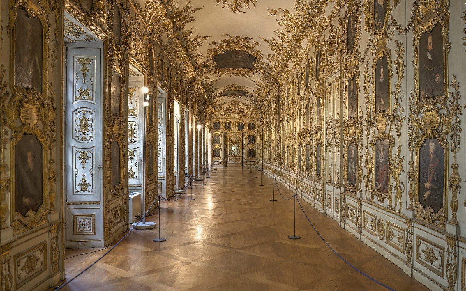 Ornate gilded gallery hallway lined with framed portraits along both walls