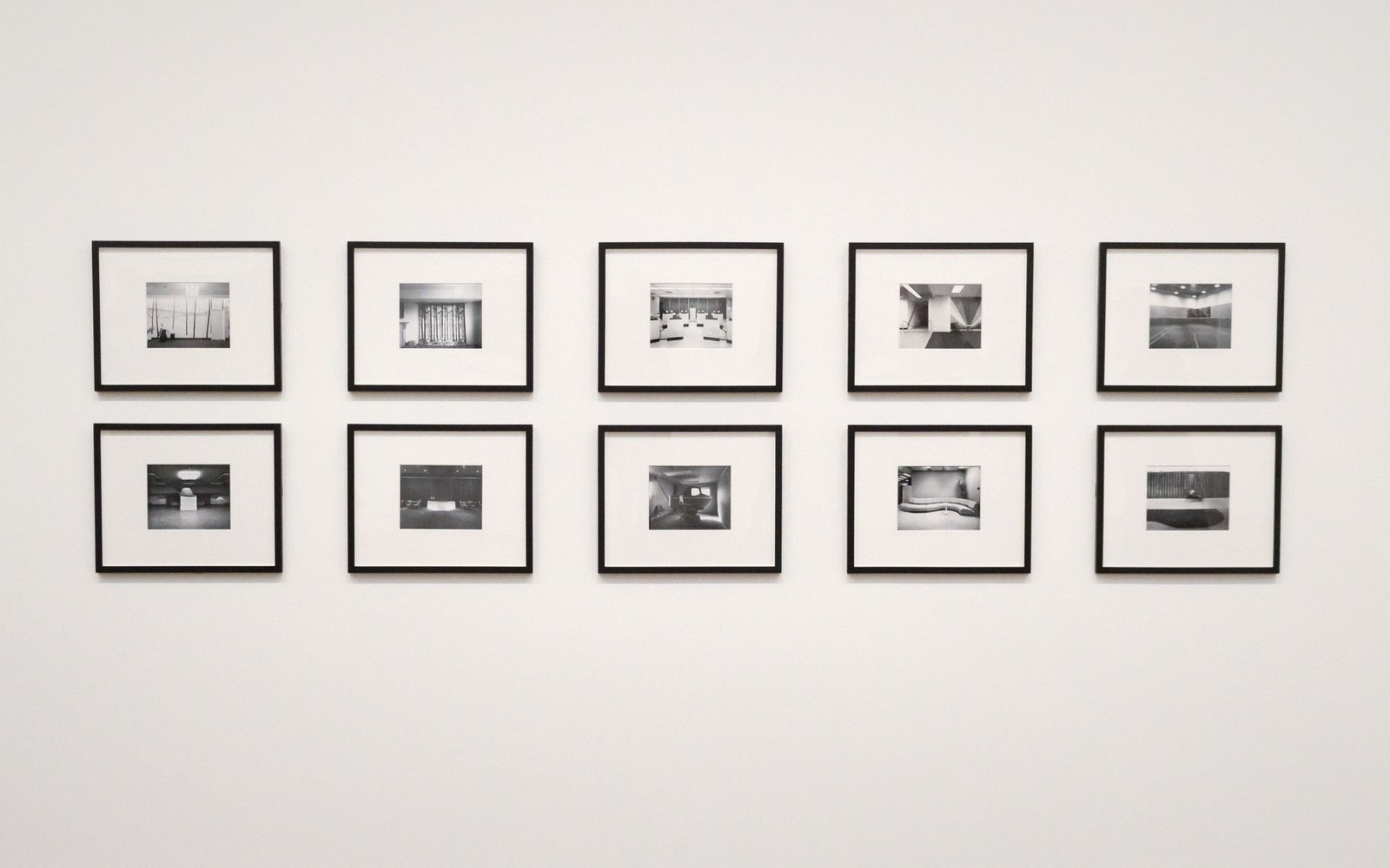 Ten black-and-white framed photographs arranged in two evenly spaced rows on a white gallery wall