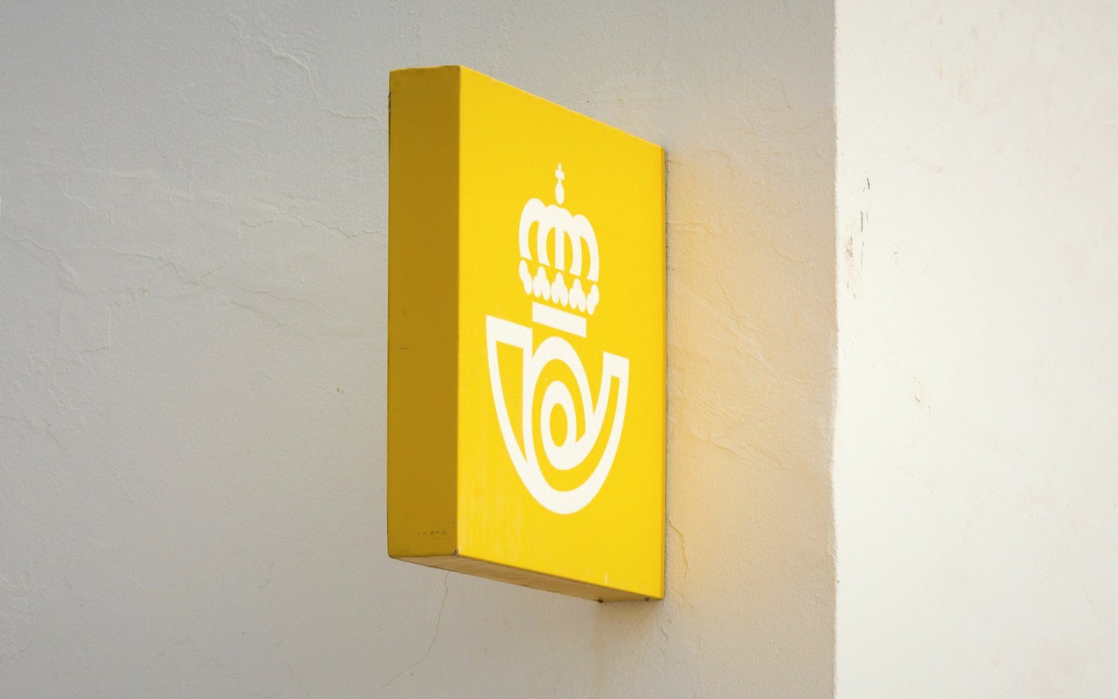 Yellow box sign with a crowned posthorn logo mounted on a white wall