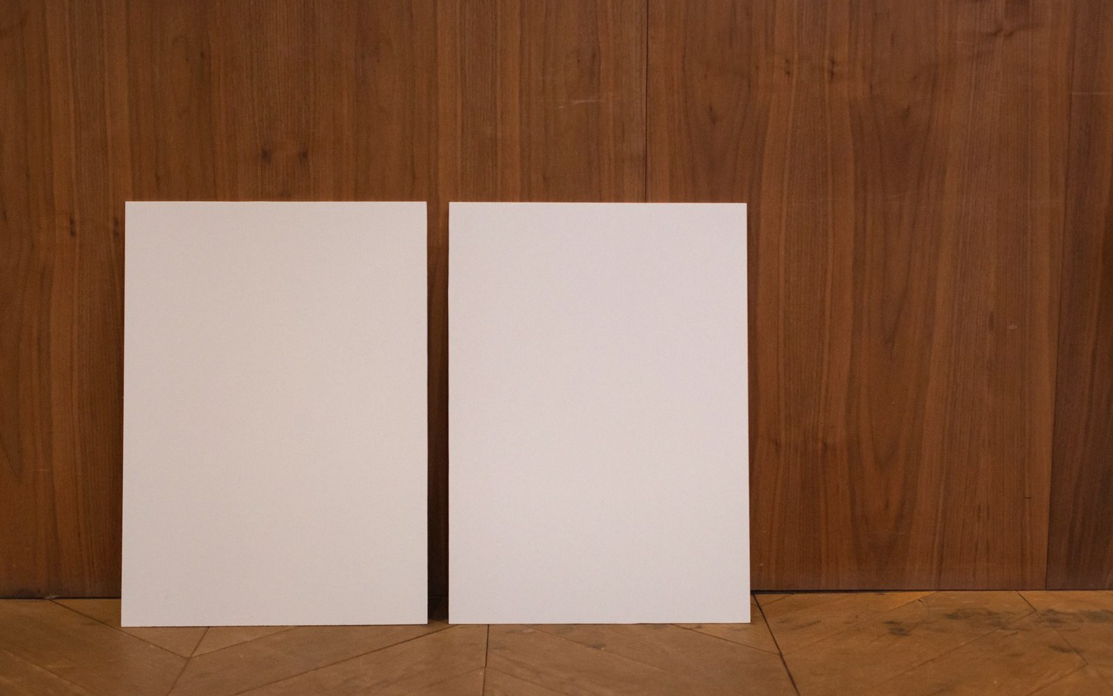 Two blank white boards leaning against a wood-paneled wall on a parquet floor